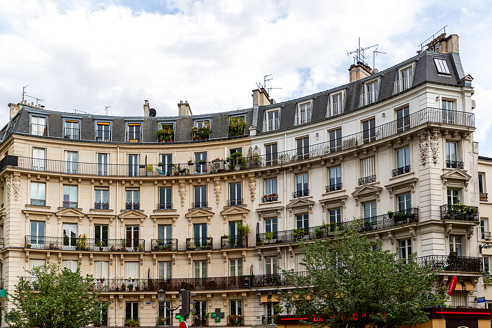 Building facade with multiple windows and balconies, featuring architectural details and plants, under an overcast sky.