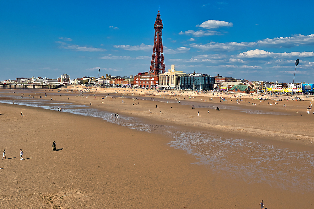 View of Blackpool beach with the Blackpool Tower rising above the cityscape on a sunny day with people enjoying the seaside.