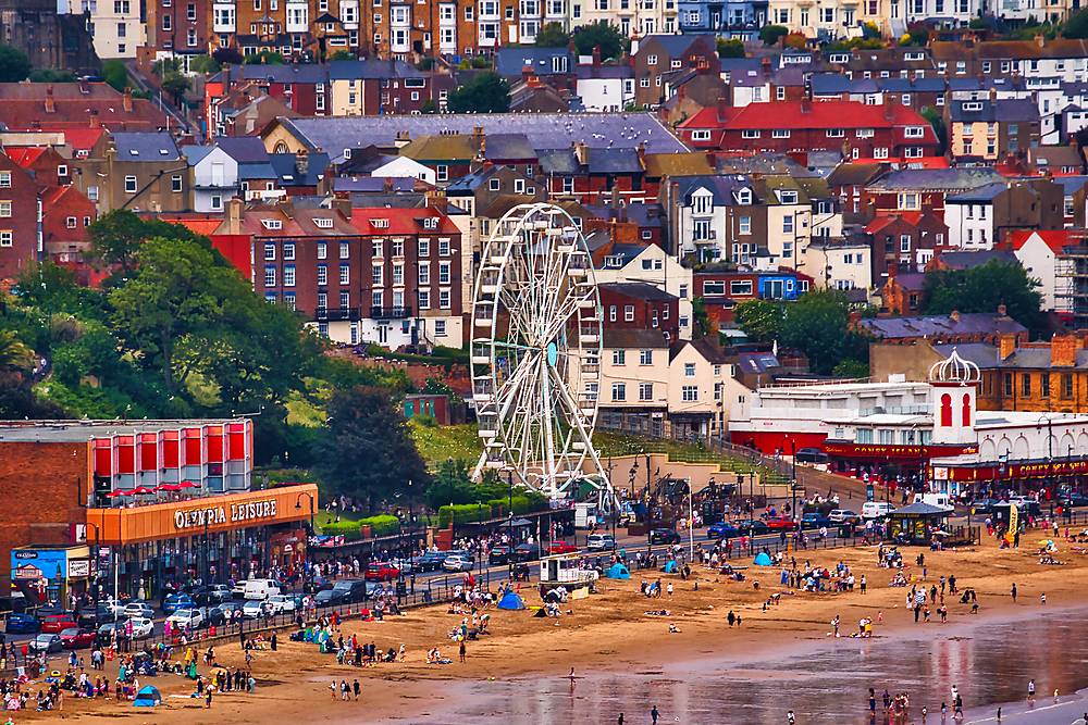 A coastal town with a beach, Ferris wheel, and numerous buildings of various heights and colors in Scarborough, UK.