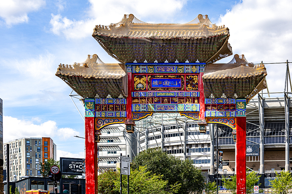 A traditional Chinese archway, adorned with intricate colorful designs and gold accents, stands prominently against a backdrop of modern urban architecture in Newcastle upon Tyne, UK.