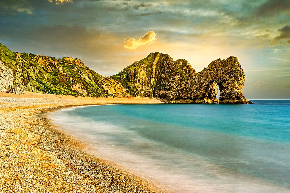 Serene beach with smooth waters, golden sand, and rugged cliffs under a sunset sky at Durdle Door, Jurassic Coast, UNESCO World Heritage Site, Dorset, England, United Kingdom, Europe