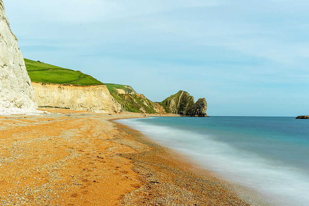 Serene beach with smooth water, sandy shore, and rugged cliffs under a clear sky at Durdle Door, Jurassic Coast, UNESCO World Heritage Site, Dorset, England, United Kingdom, Europe