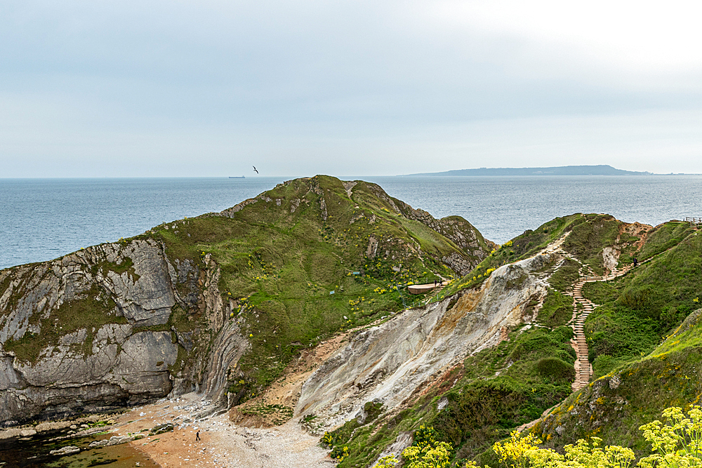 Coastal landscape with rugged cliffs, green vegetation, and a view of the ocean under a cloudy sky at Durdle Door, Jurassic Coast, UNESCO World Heritage Site, Dorset, England, United Kingdom, Europe