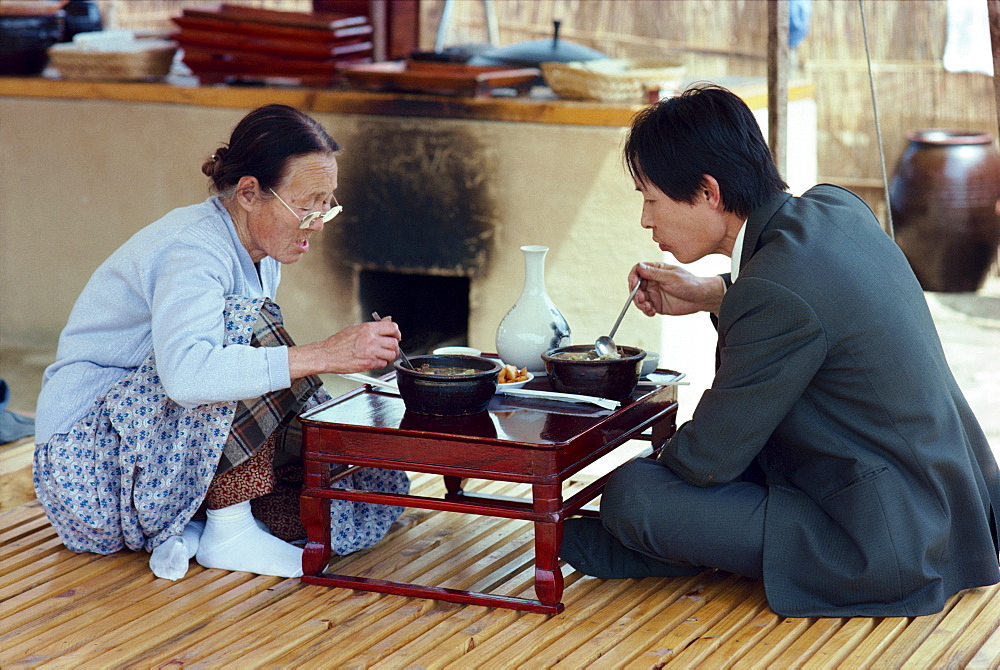 Two people eating food from a low table in the restaurant area of Folk Village in South Korea, Asia