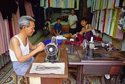 Tailor working at a sewing machine, and his family, in their shop in the old quarter of Hanoi, Vietnam, Indochina, Southeast Asia, Asia