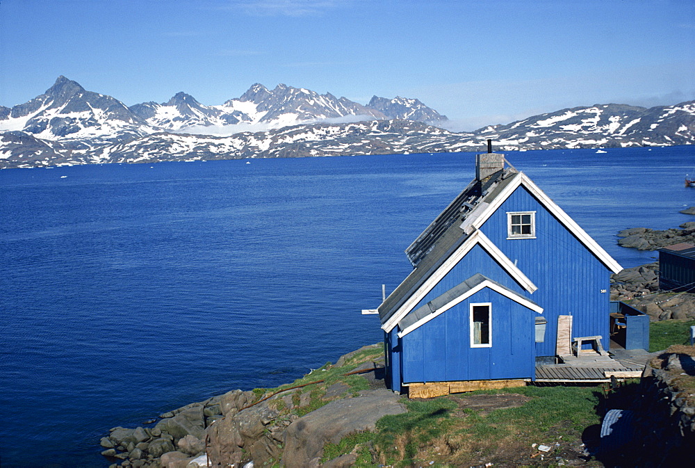 Blue painted wooden house on the coast, with mountains in the background, at Ammassalik, Greenland, Polar Regions