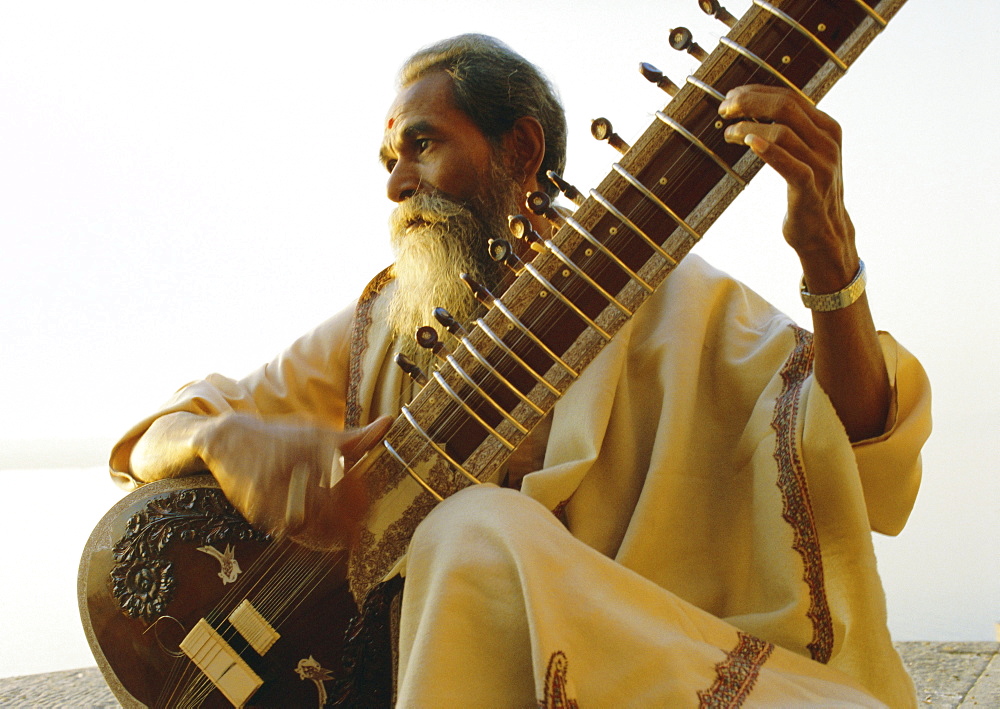 Elderly man playing a sitar by the Ganges (Ganga) River, Varanasi (Benares), Uttar Pradesh State, India