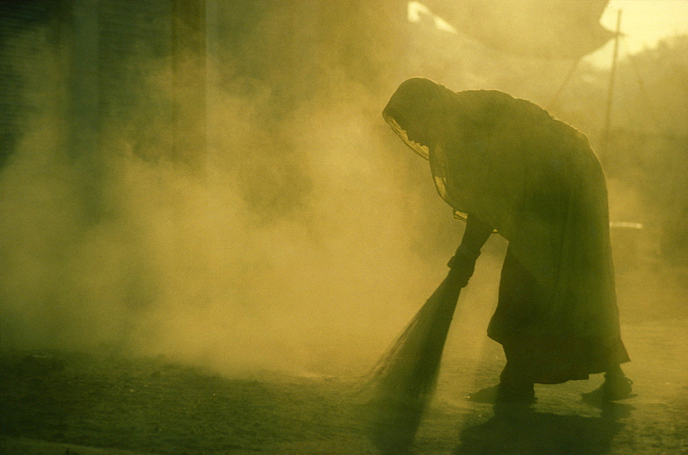 Women silhouetted at dusk, sweeping floor with brush, India, Asia