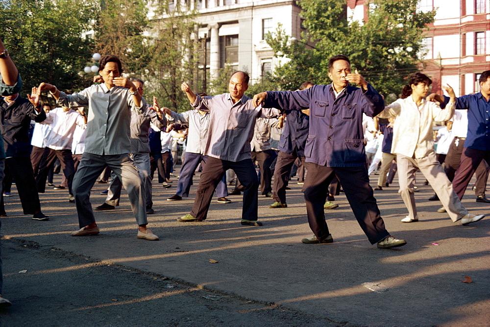 A group of men and women doing tai-chi exercises in the open air on the Bund in Shanghai, China, Asia