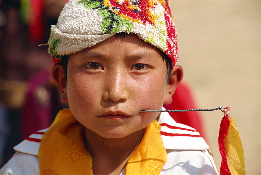 Portrait of a Tibetan boy with needle inserted in his cheek, during Harvest Festival, Coming of Age, in Qinghai, China, Asia