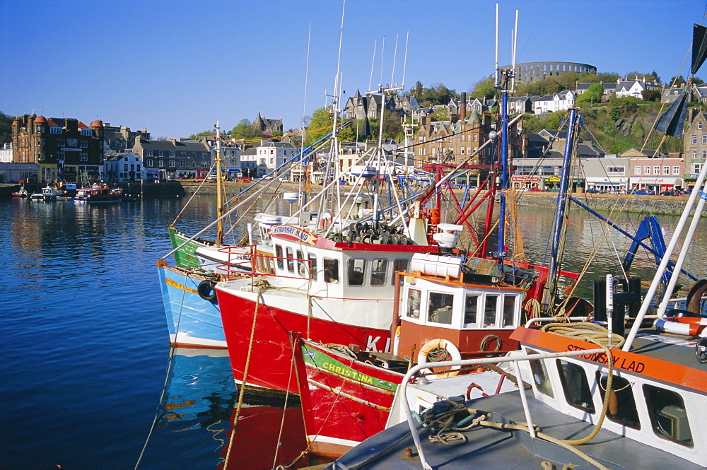 Fishing boats and waterfront with McCaig's Tower on hill, Argyll, Scotland, UK, Europe