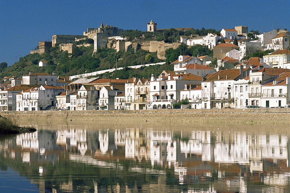 View of town and castle ramparts, reflected in Sado River, Alcacer do Sal, Portugal, Europe