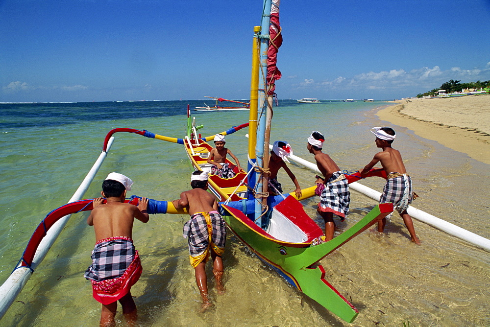 Men launching an outrigger fishing boat from Sanur Beach on the island of Bali, Indonesia, Southeast Asia, Asia