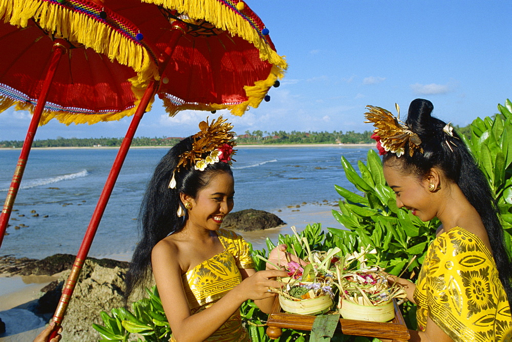 Two women prepare an offering to the sea at Jimbaran Beach on the island of Bali, Indonesia, Southeast Asia, Asia