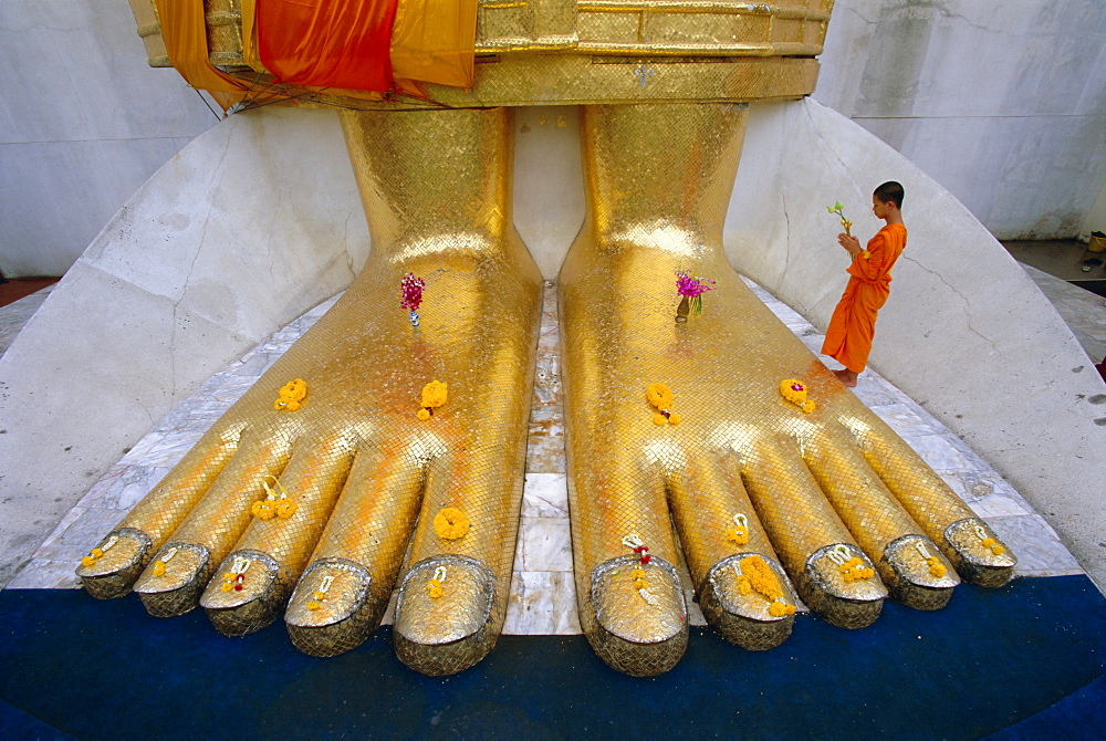 Novice monk praying at the feet of Giant Buddha statue, Wat Intharawihan (Wat In), Bangkok, Thailand, Asia