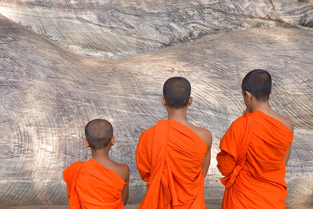 Three young monks praying at a rock-cut image of the Buddha in the Gal Vihara, Polonnaruwa (Polonnaruva), UNESCO World Heritage Site, Sri Lanka, Asia