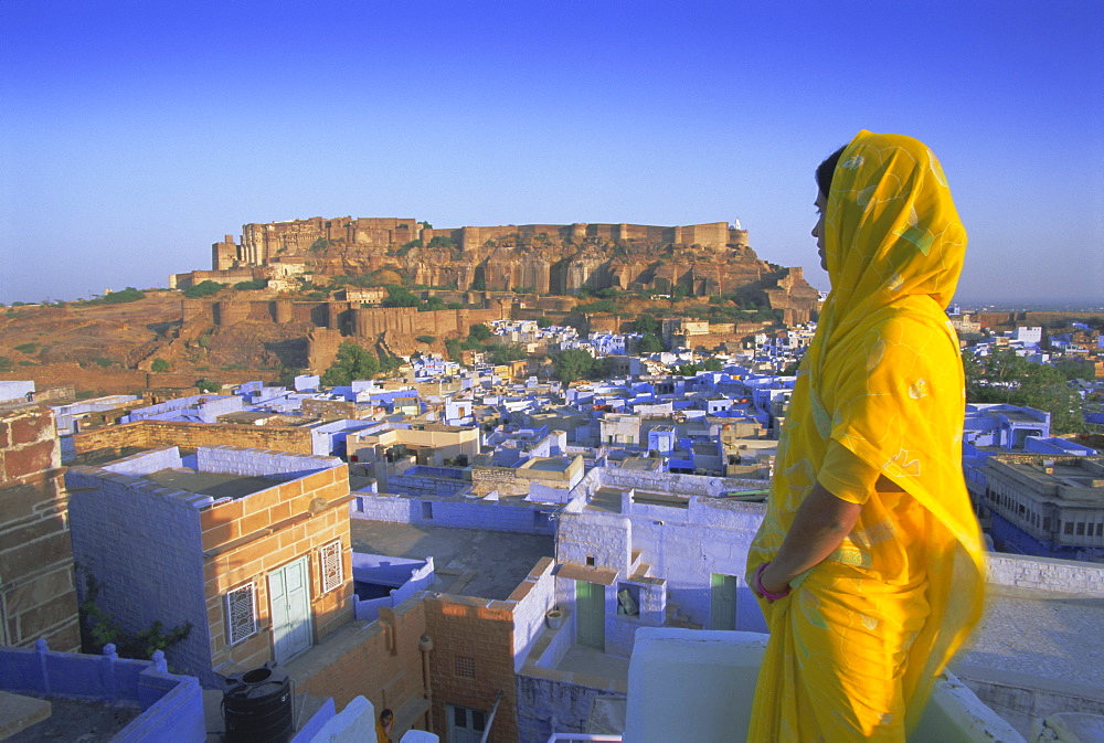 A woman in a yellow sari looking out over the 'Blue city' and fort, Jodhpur, Rajasthan State, India, Asia