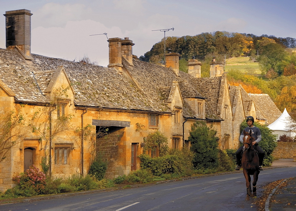 Horse and rider passing honey coloured stone cottages in the village of Stanton, The Cotswolds, Gloucestershire, England, United Kingdom, Europe