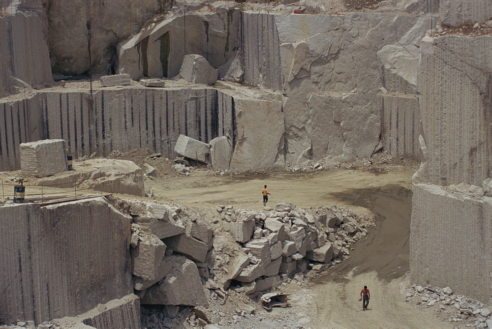 Men walking past clean faces for block extraction in granite quarry, Budduro, Sardinia, Italy, Europe