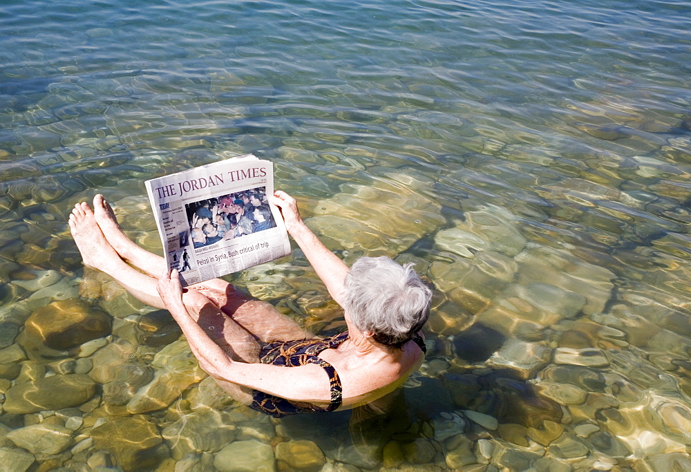 Reading newspaper floating in Dead Sea, Jordan, Middle East