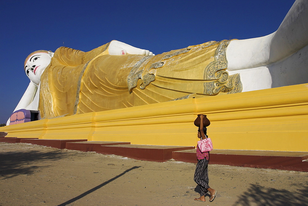 Woman walking past one of the largest reclining Buddha statues in the world, said to contain 9000 Buddha images inside, built in 1991, Monywa, Sagaing Division, Myanmar (Burma), Asia