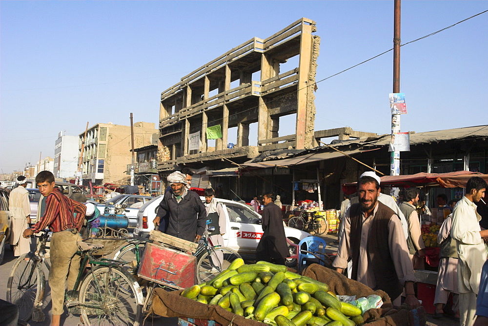 Man selling cucumbers from wheel barrow in street near war damaged building, Central Kabul, Afghanistan, Asia