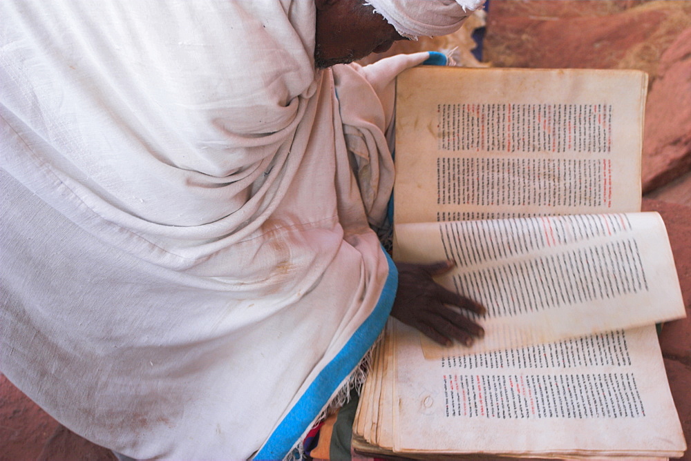 Pilgrim reading religious book on church steps, Lalibela, Ethiopia, Africa