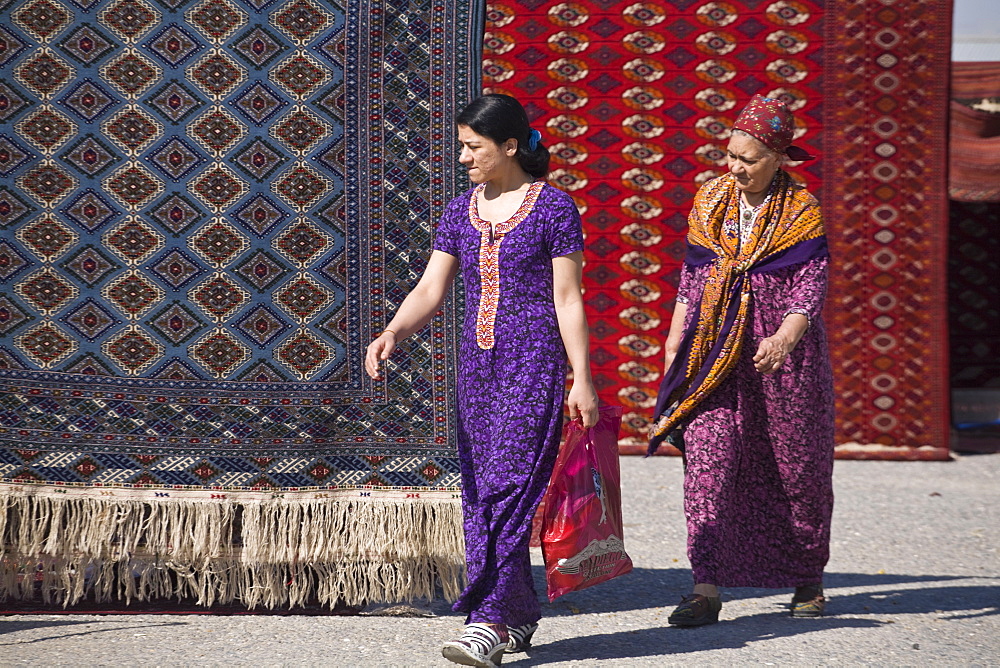 Women walking past carpets, Tolkuchka Bazaar, Turkmenistan, Central Asia, Asia