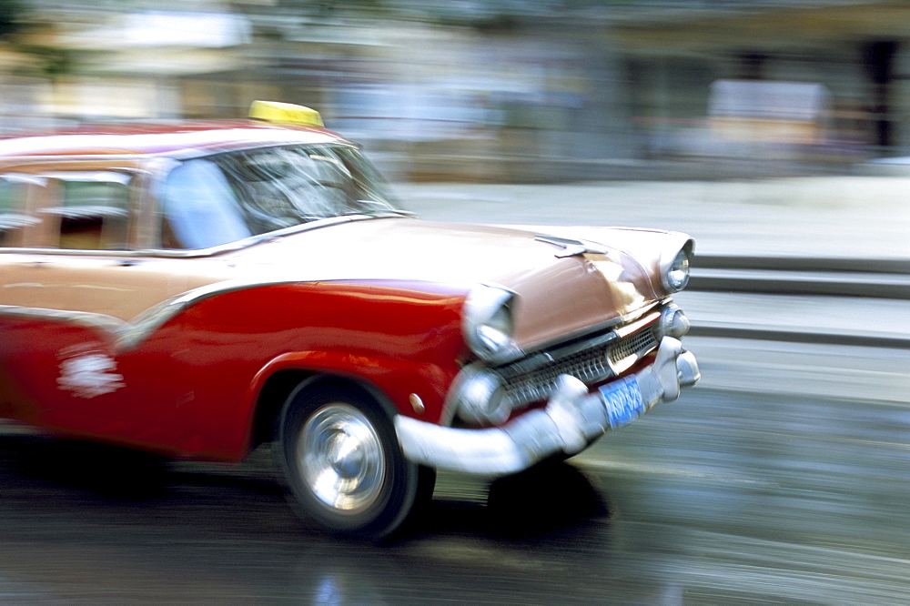 Panned shot of old American car splashing through puddle on Prado, Havana, Cuba, West Indies, Central America 