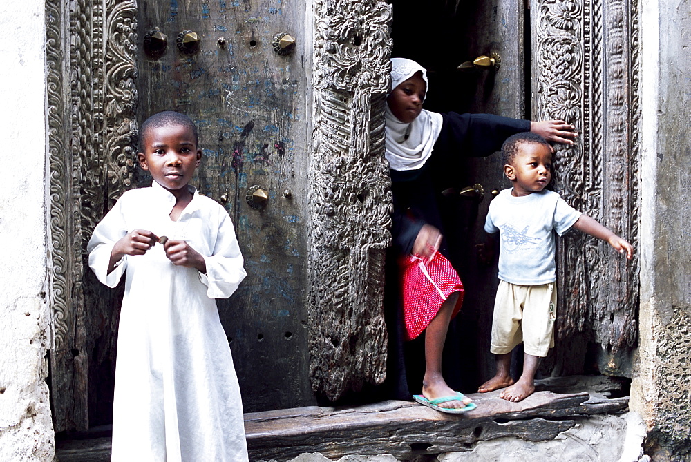 Young Muslim children in front of an ornate carved door, Stone Town, Zanzibar, Tanzania, Africa