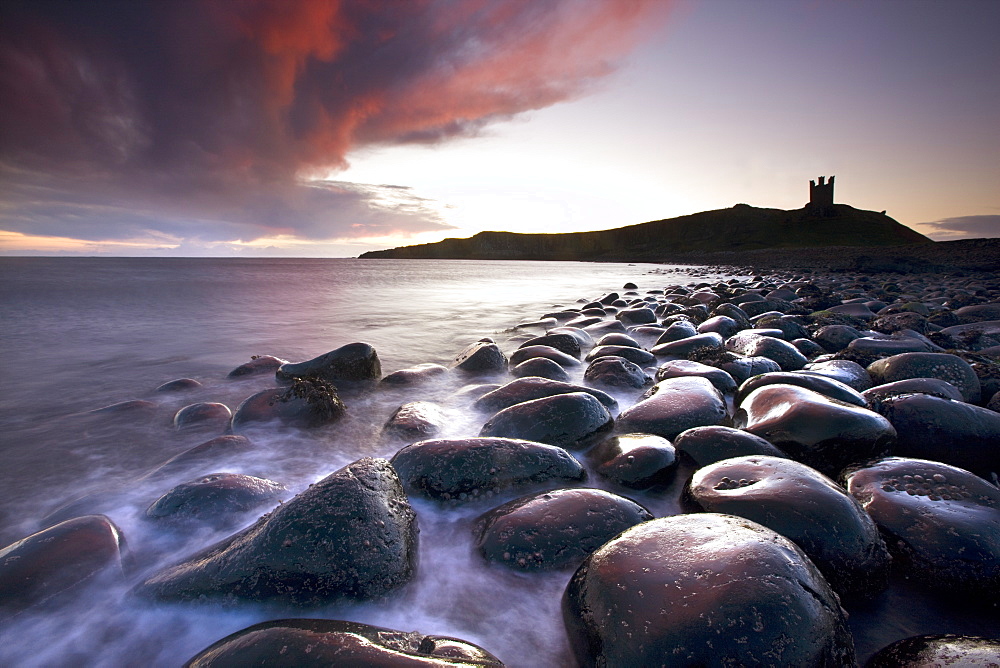 Dawn over Embleton Bay with basalt boulders in the foreground and the ruins of Dunstanburgh Castle in the background, near Alnwick, Northumberland, England, United Kingdom, Europe