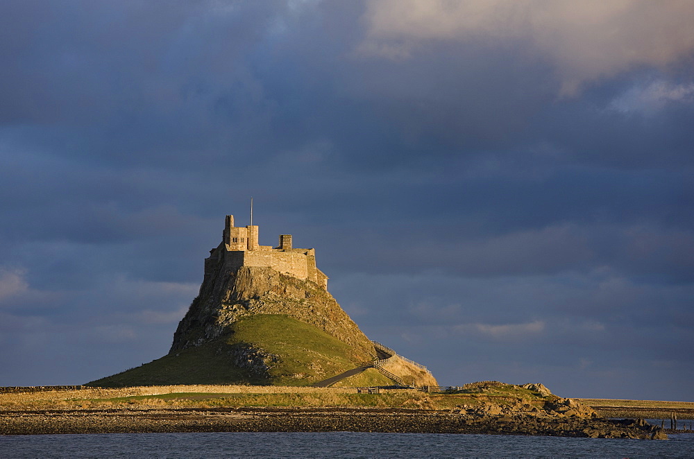 Lindisfarne Castle bathed in afternoon sunlight against a stormy sky, Holy Island. Northumberland, England, United Kingdom, Europe