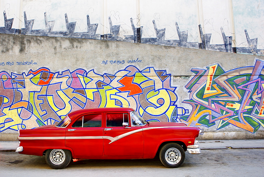 Classic red American car parked in front of grafitti covered wall, Havana, Cuba, West Indies, Central America