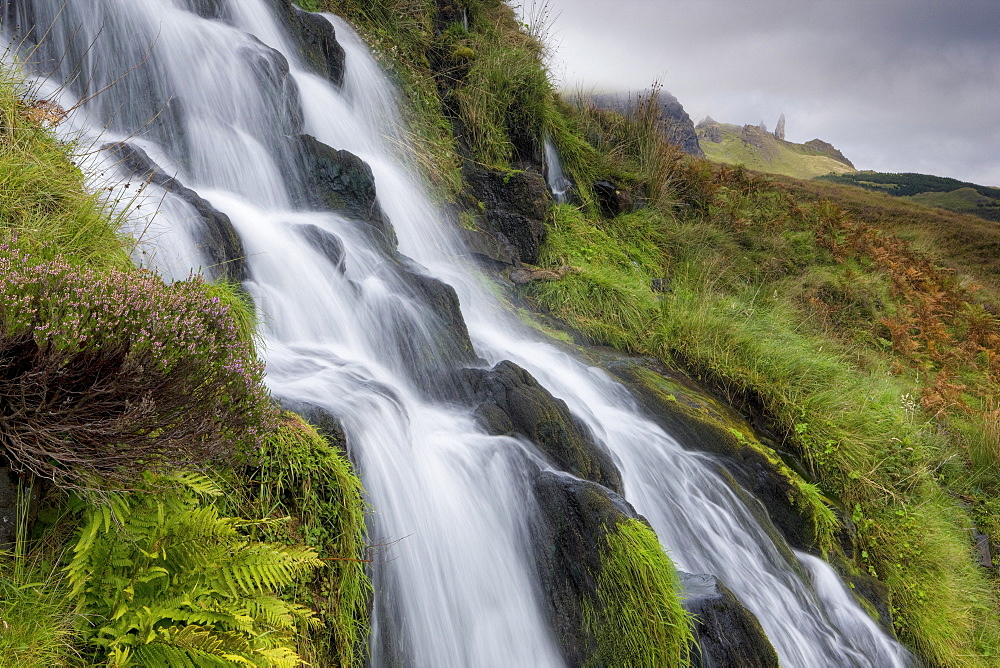 Waterfall cascading down grassy slope with Old Man of Storr in background, near Portree, Isle of Skye, Highland, Scotland, United Kingdom, Europe