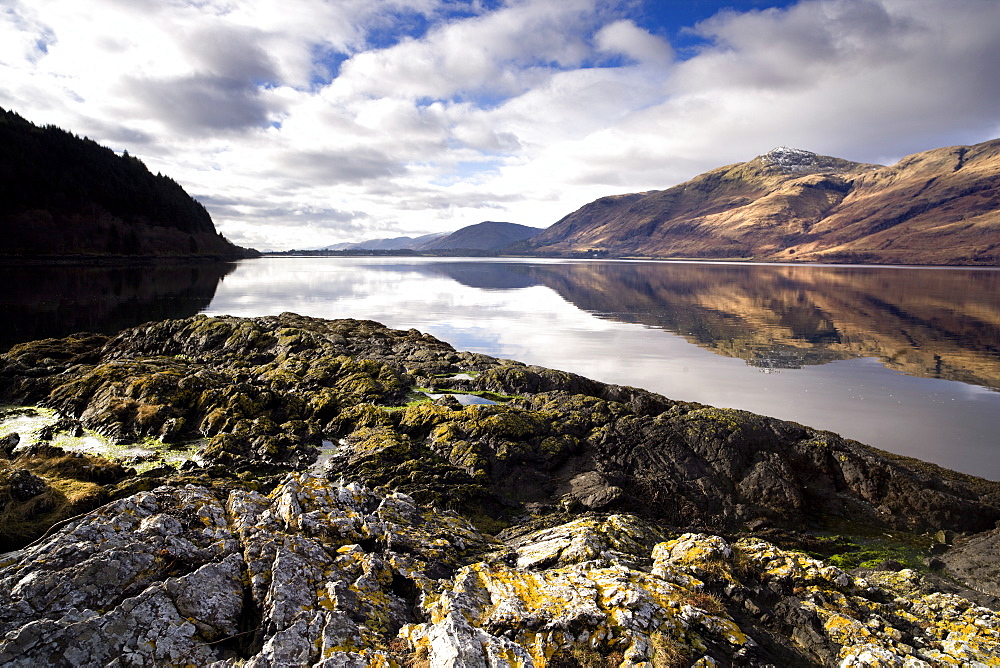 Winter view of Loch Linnhe in calm weather with reflections of distant mountains and rocky foreshore, near Fort William, Highland, Scotland, United Kingdom, Europe