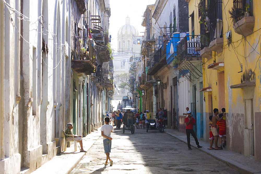 View along a typical residential street in Havana Vieja showing children playing, an old lady sitting in the sunshine and bicycle taxis carrying passengers, Havana, Cuba, West Indies, Central America