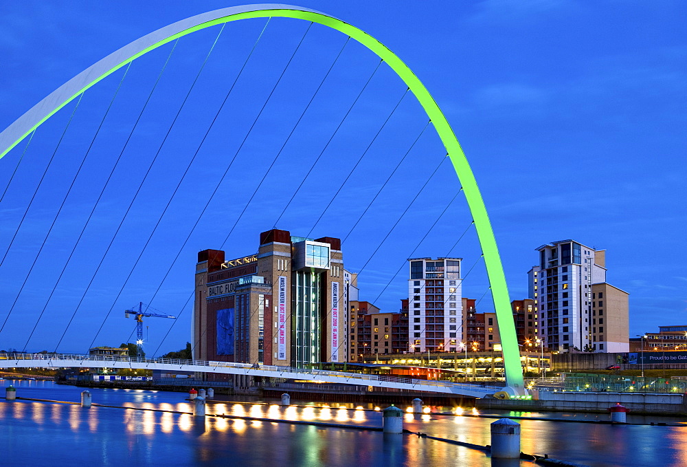 View along the Quayside at night showing the Baltic Centre for Contemporary Arts framed by the floodlit Gateshead Millennium Bridge, Newcastle-upon-Tyne, Tyne and Wear, England, United Kingdom, Europe