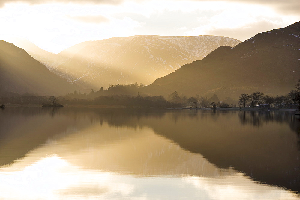 Morning sunlight bursting through clouds over fells with reflections in Lake Ullswater, near Glenridding Village, Lake District National Park, Cumbria, England, United Kingdom, Europe