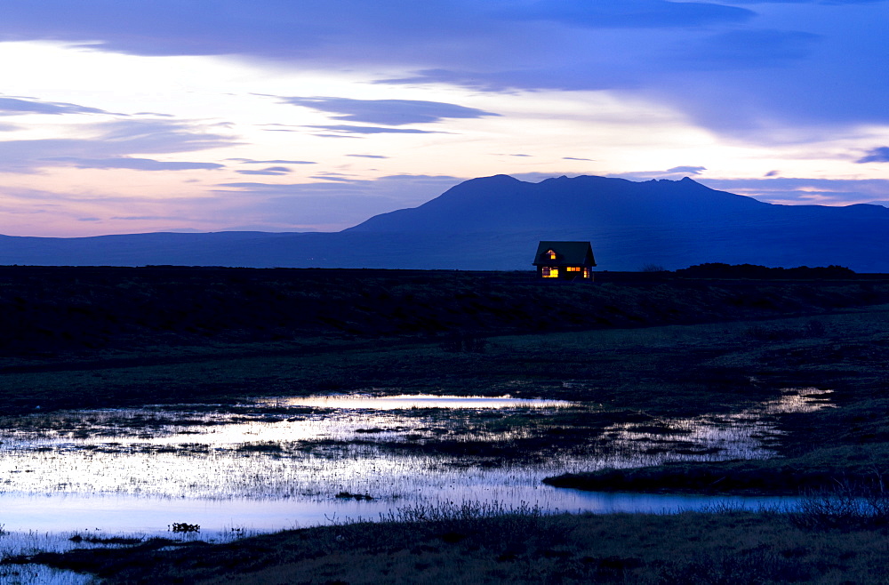 Twilight view towards mountains with small house illuminated by interior lights, near Hella, South West Iceland, Iceland, Polar Regions