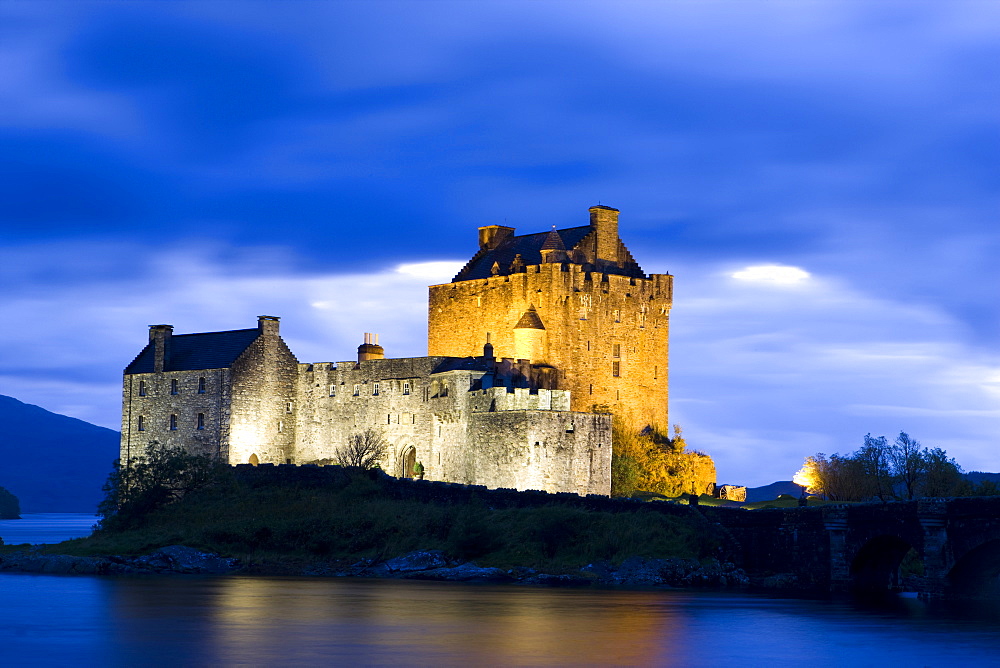 Eilean Donan Castle floodlit against deep blue twilight sky and water of Loch Duich, near Dornie, Kyle, Highlands, Scotland, United Kingdom, Europe