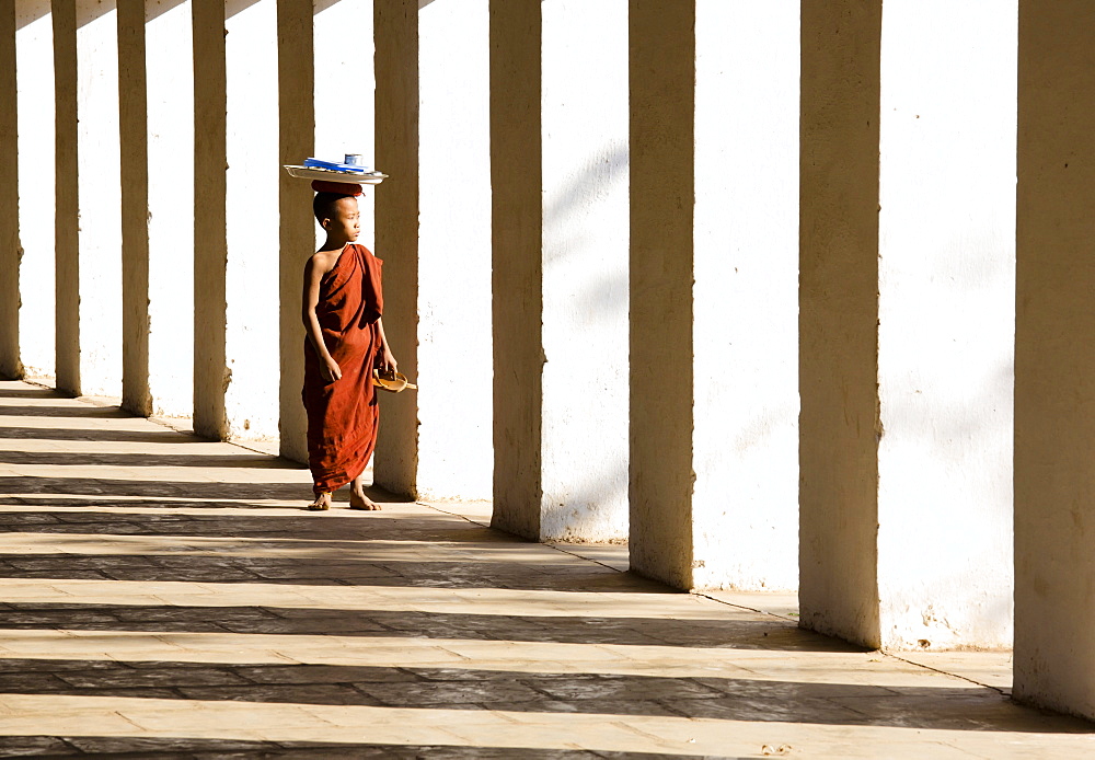 Novice Buddhist monk standing in the shadows of columns at Shwezigon Paya, Nyaung U, Bagan, Myanmar (Burma), Asia