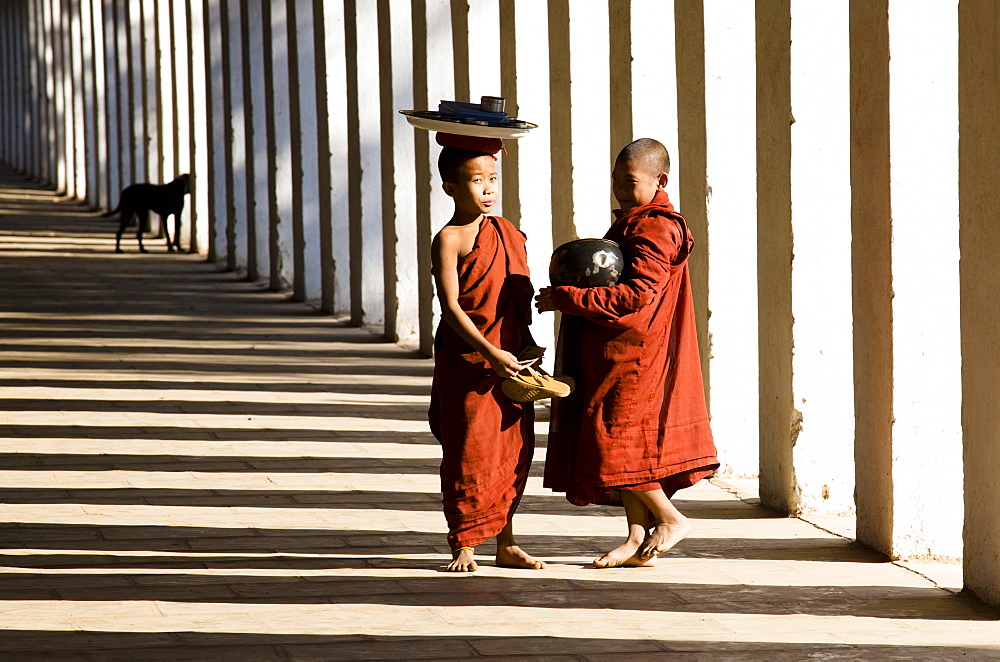 Novice Buddhist monks collecting alms, standing in the shadows of columns at Shwezigon Paya, Nyaung U, Bagan, Myanmar (Burma), Asia