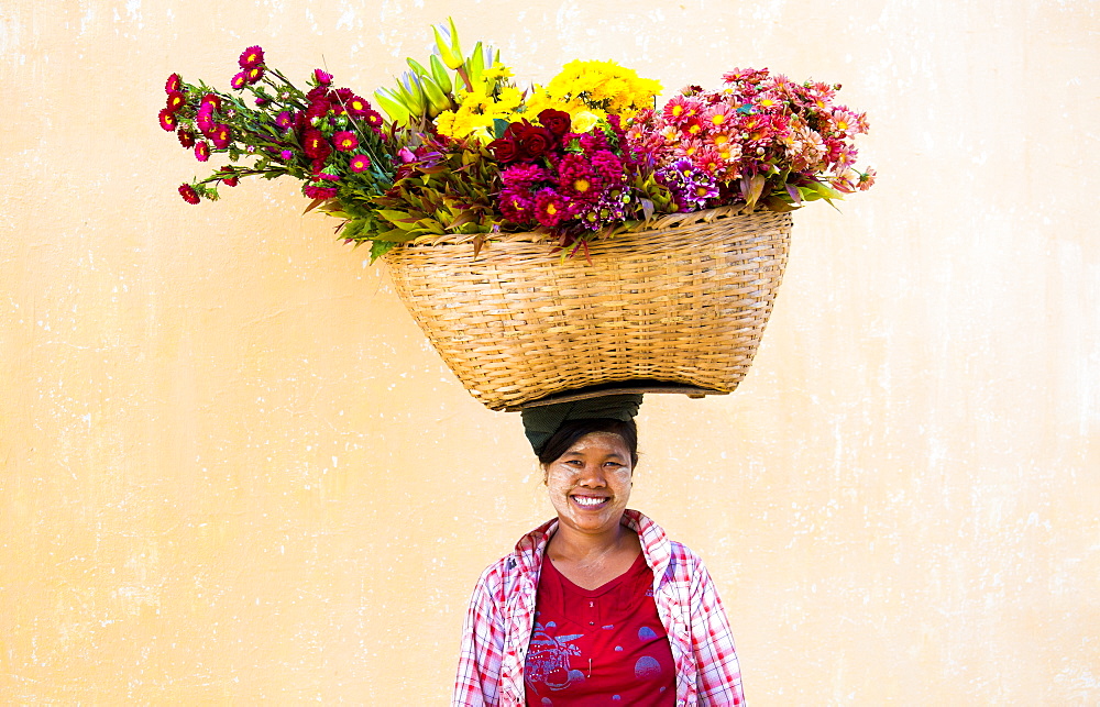 Local woman with thanakha traditional face painting, carrying a large basket of fresh flowers on her head, Shwezigon Paya, Nyaung U, Myanmar (Burma), Asia