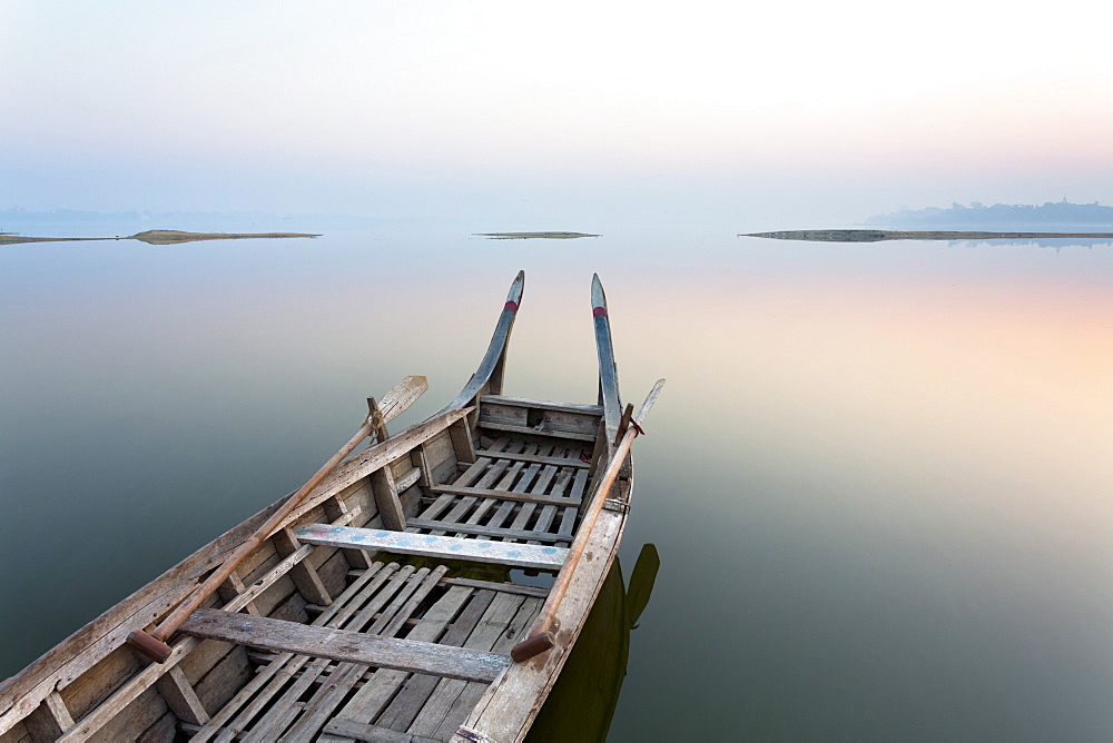 Traditional rowing boat moored on the edge of flat calm Taungthaman Lake at dawn with the colours of the sky reflecting in the calm water, close to the famous U Bein teak bridge, near Mandalay, Myanmar (Burma), Asia