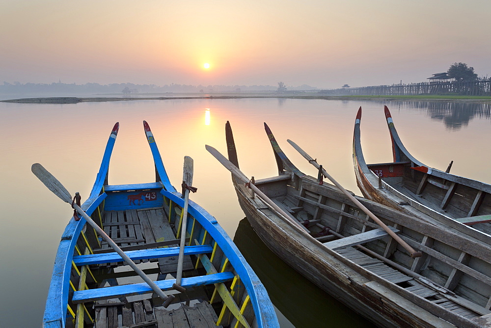 Traditional rowing boat moored on the edge of flat calm Taungthaman Lake at dawn with the colours of the sky reflecting in the calm water, close to the famous U Bein teak bridge, near Mandalay, Myanmar (Burma), Asia