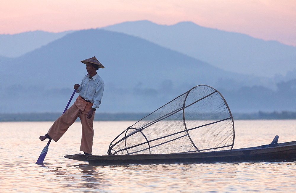 Intha 'leg rowing' fishermen at dawn on Inle Lake who row traditional wooden boats using their leg and fish using nets stretched over conical bamboo frames, Inle Lake, Myanmar (Burma), Southeast Asia