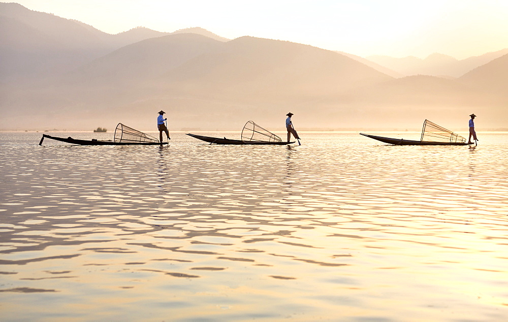 Intha 'leg rowing' fishermen at sunset on Inle Lake who row traditional wooden boats using their leg and fish using nets stretched over conical bamboo frames, Inle Lake, Myanmar (Burma), Southeast Asia