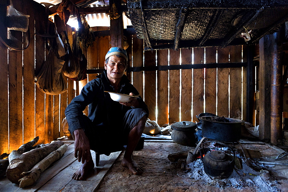 Animist man of the Ann tribe eating in his home by open fire, Panlor village, near Kengtung (Kyaingtong), Shan State, Myanmar (Burma), Asia