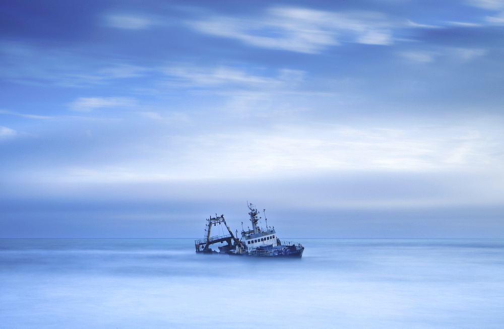 Shipwreck off the Atlantic coast, shot with long exposure to record motion in sea and sky, near Walvis Bay, Namibia, Africa