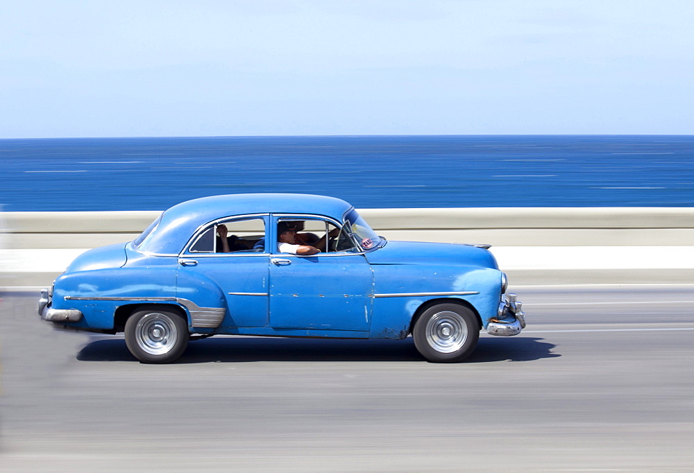 Panned' shot of old blue American car to capture sense of movement, with the Caribbean Sea in the background, The Malecon, Havana Centro, Cuba, West Indies, Central America